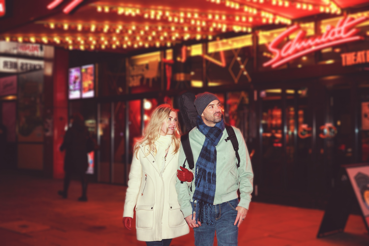 Two people standing on a street at night with neon signs in the background