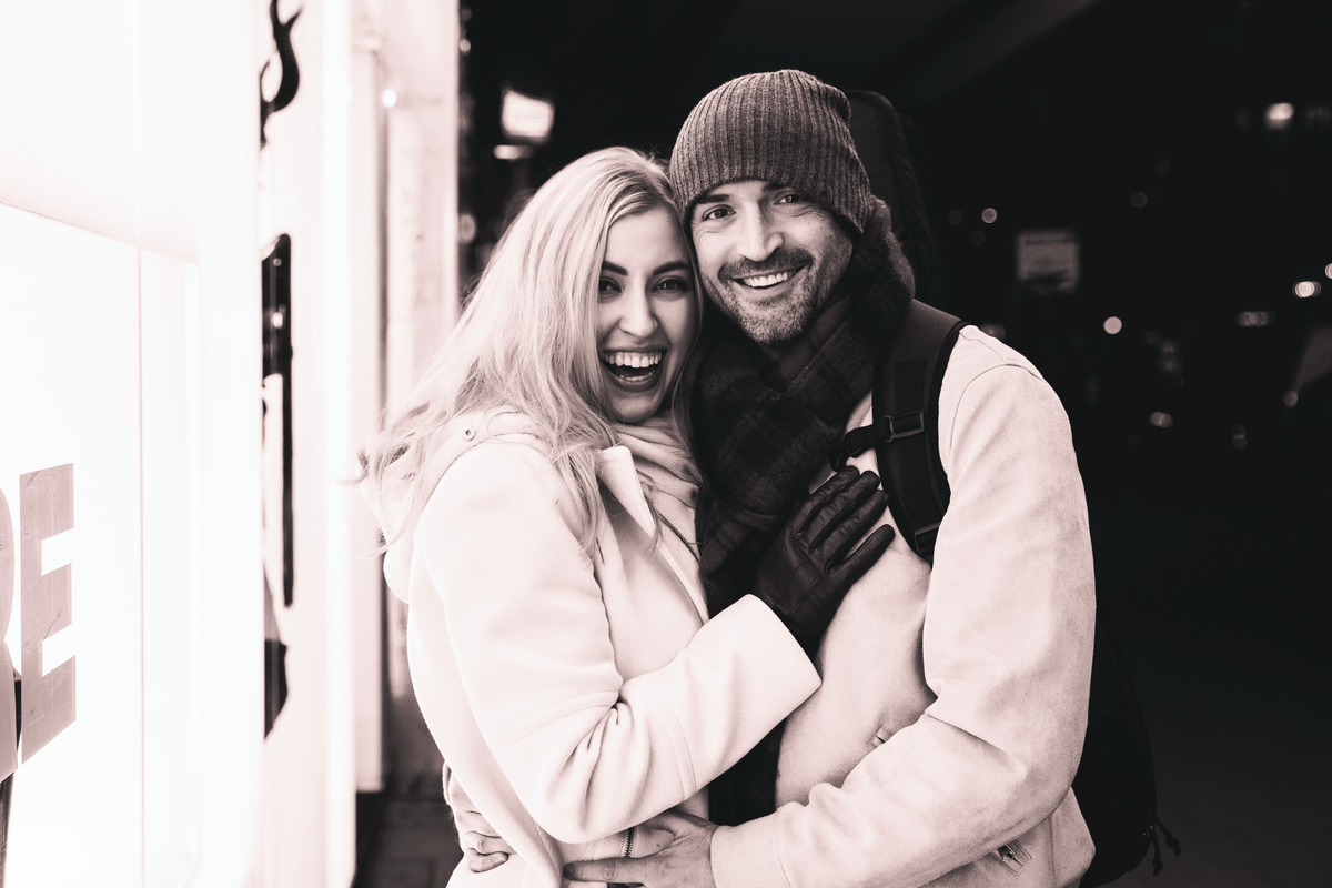 Black and white photo of a couple hugging in front of a store window.